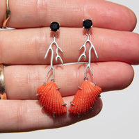 Shell-shaped earrings with black gemstones on a hand against a neutral background