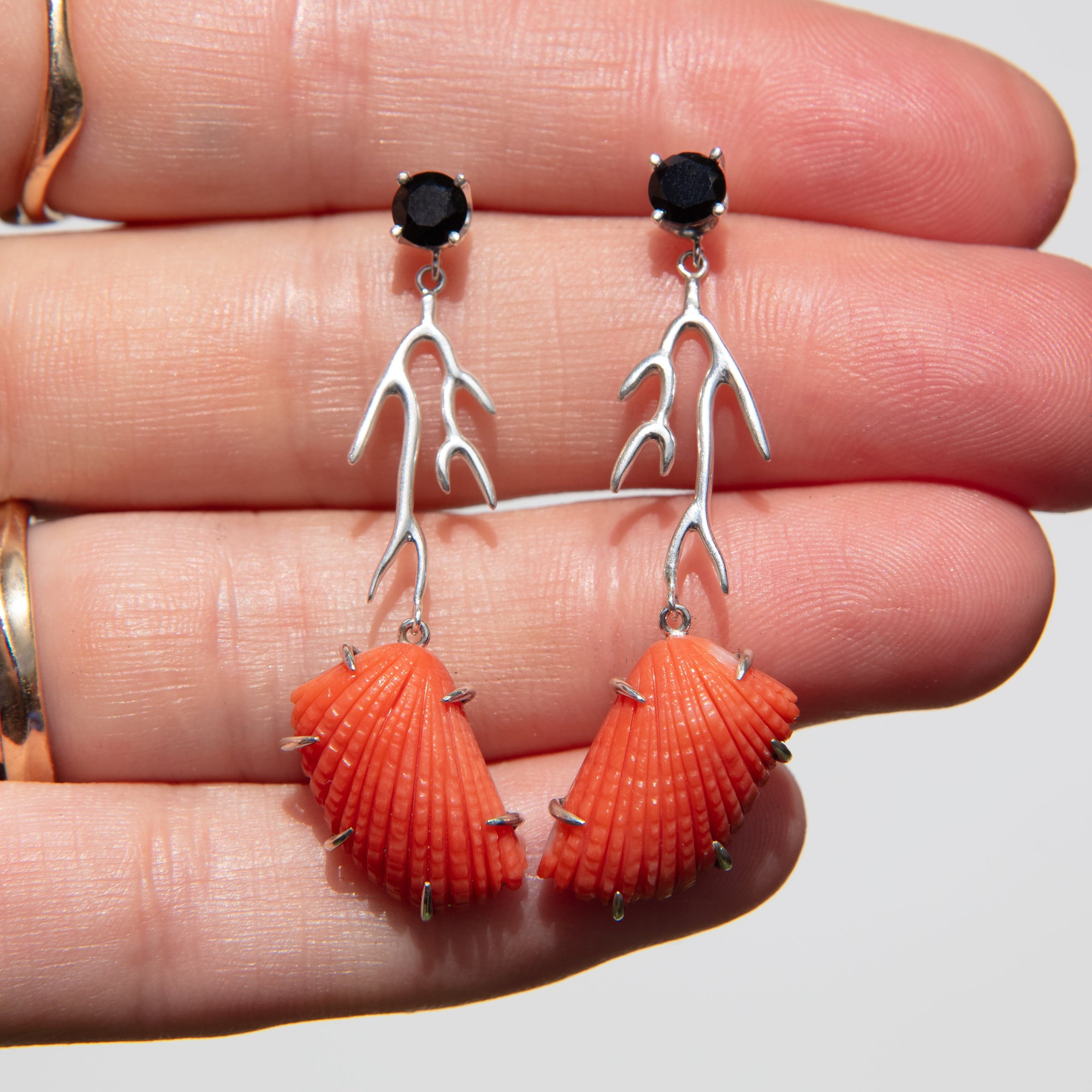 Shell-shaped earrings with black gemstones on a hand against a neutral background