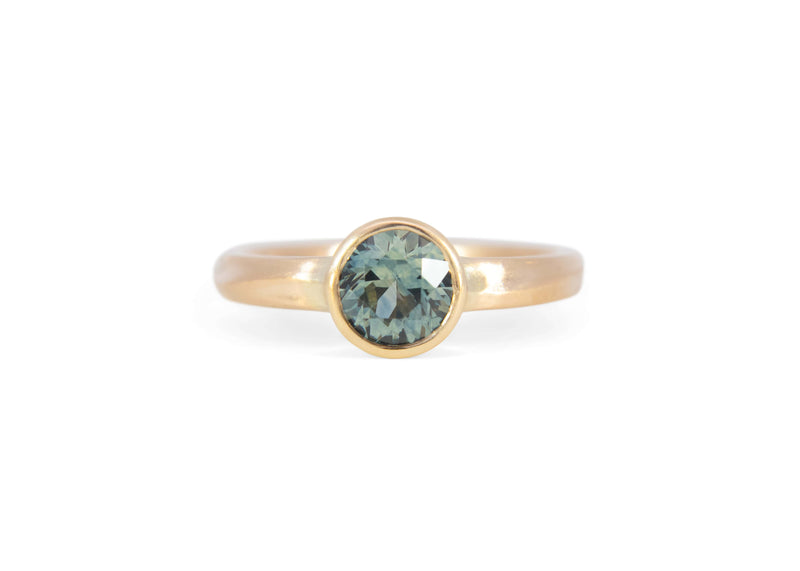 Gold solitaire ring with a teal montana sapphire on a white background