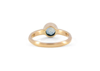 back of a gold solitaire ring with a teal montana sapphire against a white background