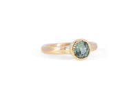 Gold solitaire engagement ring with a teal montana sapphire on a white background