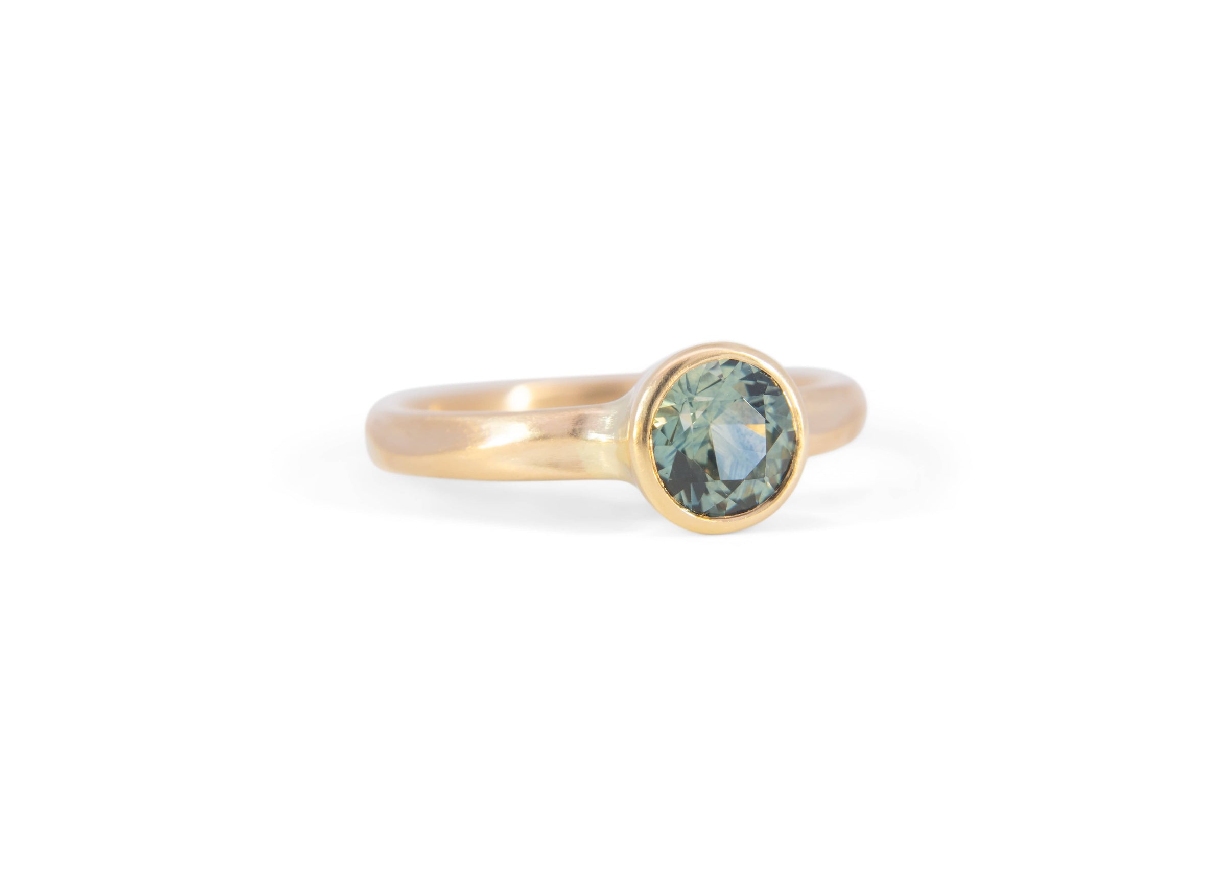Gold solitaire engagement ring with a teal montana sapphire on a white background