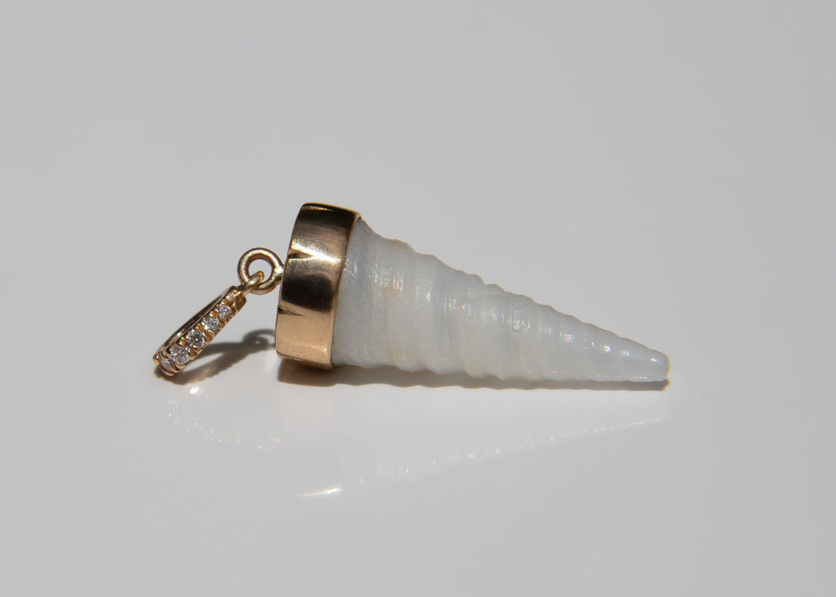 A spiral cone-shaped shell pendant with a polished gold cap and a small gold diamond-studded bail at the top, shown on a reflective light gray surface.