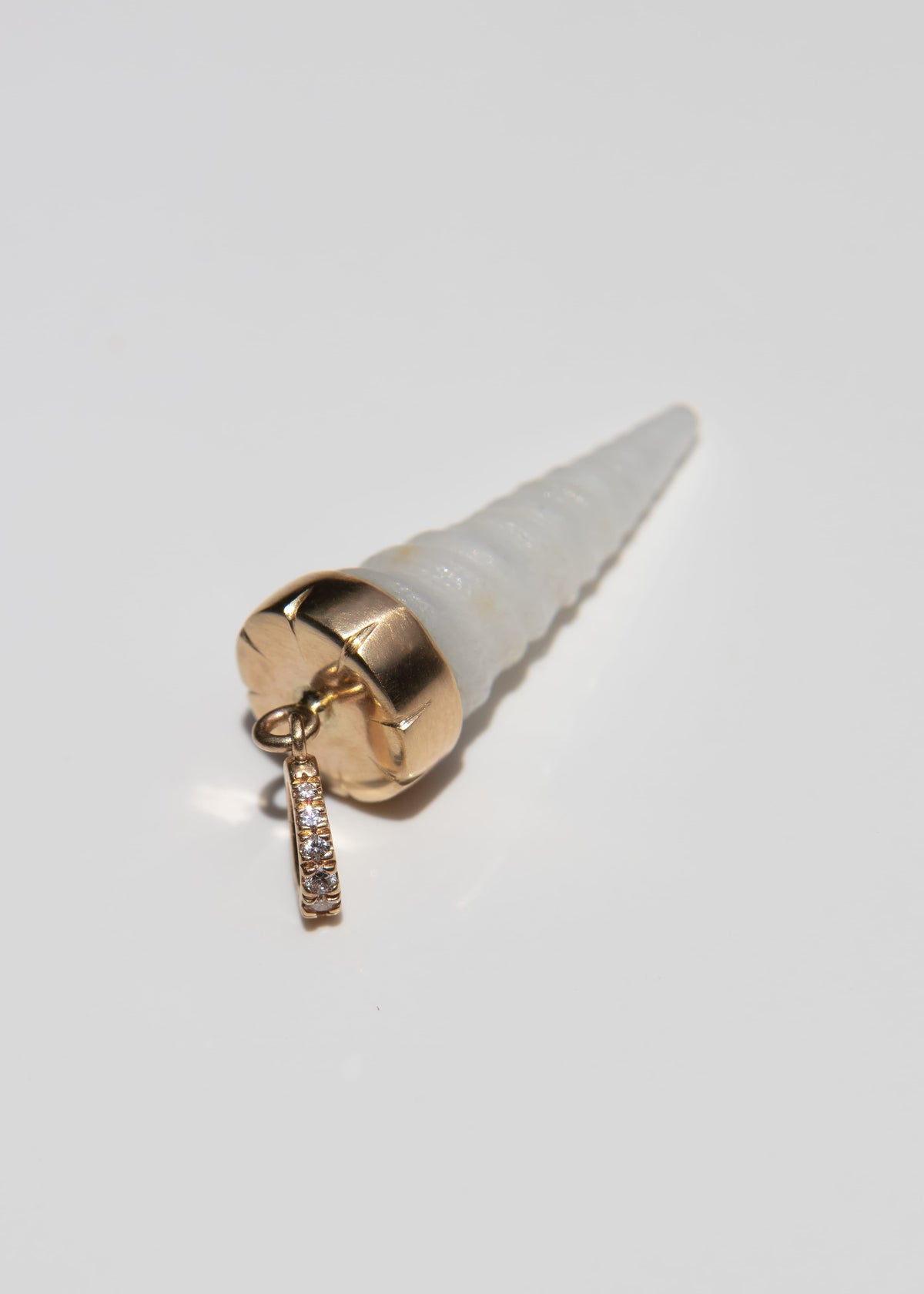 A cone-shaped shell pendant charm with a textured off-white body, a polished gold-toned base, and a small gold diamond-studded bail at the top, shown on a plain light gray background.