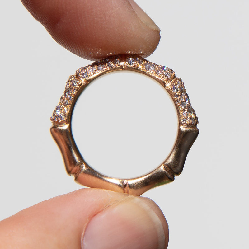 Gold bamboo ring with pave set diamonds held between fingers against a neutral background