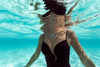 model in black one piece bathing suit wearing seafoam blue urchin inspired necklace underwater