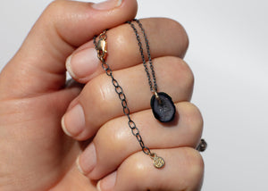 gray and black tabasco geode necklace on oxidized silver chain and gold clasp in hand